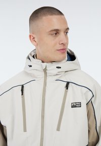 Witte waterdichte jas met een hoge kraag, contrasterende beige accenten en twee ritszakken aan de voorkant, met een logo op de borst.