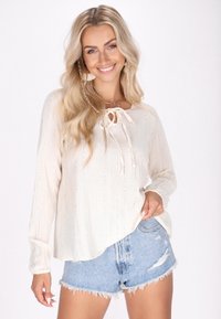 Cremefarvet top med lange ærmer, bånd-hals detalje, diskrete lodrette striber, parret med slidte denim shorts.