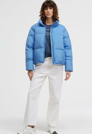 Blue puffer jacket with a high collar, featuring a quilted design. Paired with white wide-leg pants and gray sneakers.