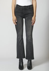 Jeans de mezclilla negra acampanada con una textura descolorida, que presentan acentos con tachuelas en los bolsillos delanteros y un diseño clásico de cinco bolsillos.