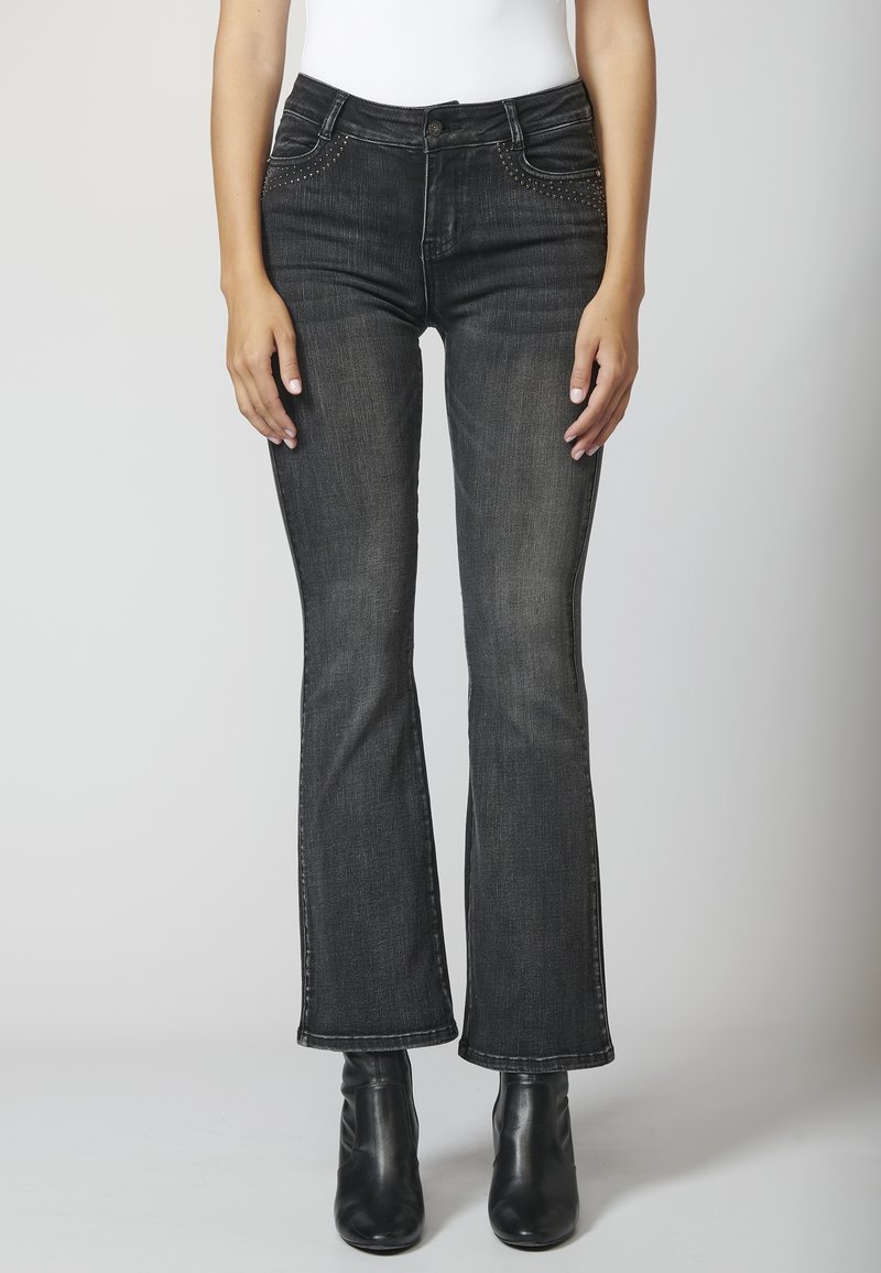 Jeans de mezclilla negra acampanada con una textura descolorida, que presentan acentos con tachuelas en los bolsillos delanteros y un diseño clásico de cinco bolsillos.