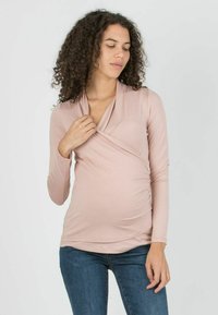 Light pink, long-sleeve wrap top with a v-neck design and ruched side detailing, made from a soft, stretchy fabric.