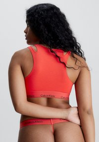 Calvin Klein röd bralette med urklippta axeldetaljer, sömlös design och matchande röd stringtrosa med logoband i midjan.