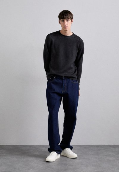 Dark gray knitted sweater with a round neckline, paired with loose blue jeans. Model wears white sneakers. Simple, clean design.