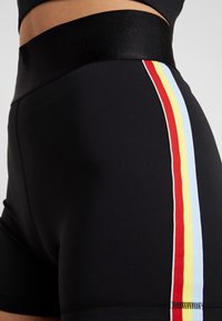 Pantaloni sportivi neri con una vita ampia, caratterizzati da strisce verticali in rosso, giallo e blu lungo il lato. Texture liscia.