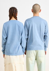 Light blue long-sleeve shirts with rounded necklines, made of soft fabric, viewed from the back on two individuals.