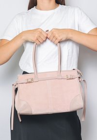 Borsa in suede rosa blush con doppio manico superiore, cinturino sottile rimovibile, dettagli in hardware dorato e cuciture decorative.