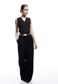 CzarnaCropowana kamizelka z dekoltem w kształcie litery V i pięcioma guzikami, zestawiona z szerokimi czarnymi spodniami. Gładki materiał, elegancki design i dopasowany krój.