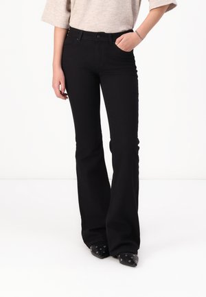 Jeans évasés noirs en denim avec une texture lisse. Comprend cinq poches et une fermeture à bouton à l'avant. Portés avec des chaussures noires à talons pointus.