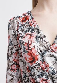 Top avvolgente floreale con un mix di fiori rossi, grigi e neri su uno sfondo chiaro; realizzato in tessuto testurizzato con scollatura a V.