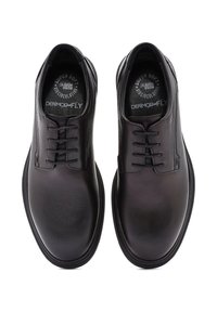 Chaussures en cuir noir avec une texture lisse, un design à cinq œillets et un bout arrondi. Marquage de la semelle intérieure visible.