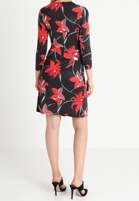 Svart klänning med röd blommönster och gröna stjälkar, med långa ärmar och en figurnära design. Bärs med svarta klackar.