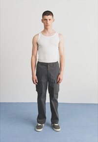 Grå cargo bukser med flere lommer, iført en hvid tank top og grå sneakers. Modellen står mod en ensfarvet baggrund.