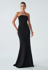 Melnas strapless kleitas ar pieguļošu augšdaļu un izplestu svārku. Izgatavota no gludas auduma, ar tīrām līnijām un minimālu dekorēšanu.