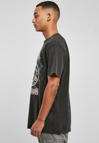 Black cotton t-shirt with a loose fit, short sleeves, and a graphic design featuring colorful text and abstract patterns on the front.
