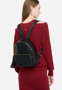 Nais, kellel on seljas burgundia värvi kudum dress, millel on avatud õlad ja väike must nahast seljakott, millel on kuldsed lukud ja tillukesed nöörid.