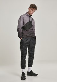 Sort sporty jakke med grå gradient, lynlås krave; sorte bukser; sort crossbody taske; sorte sneakers; hvide sokker. Glat finish.