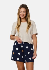 Beżowy prążkowany T-shirt zestawiony z granatowymi szortami w dużą białą i brązową kropkę. Strój ma luźny krój i swobodny styl.