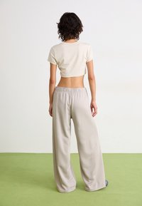T-shirt blanche coupée et pantalon beige ample. Le pantalon a une taille élastique et des jambes larges. Tissu lisse avec une finition mate.
