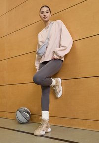 Šviesiai ruda megztinis, pilkos leginsai ir tan spalvos aukštakulniai sportbačiai su baltais padais. Šalia yra šviesiai mėlyna rankinė-per petį ir krepšinio kamuolys.