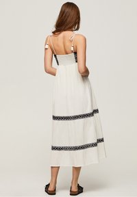 Maxikleid aus leichtem cremefarbenem Stoff mit einem geschmuggelten schwarzen Oberteil, verstellbaren Trägern und schwarzen gestickten Bändern über dem Rock.