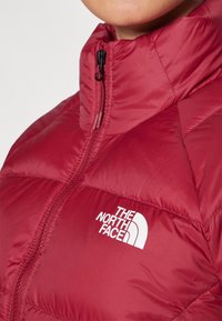 Chaqueta de plumas roja con cuello alto cerrada, con el logo blanco de The North Face en el lado izquierdo del pecho.