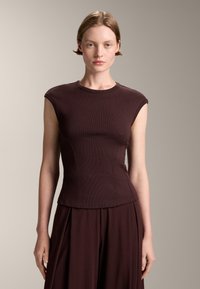 Burgundyröd figurnära ärmlös topp i ribbad textur med rund halsringning och böjda sömmar, matchad med en plisserad nederdel.