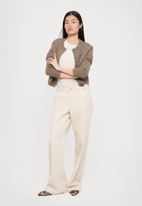 Brun strikket cardigan over en beige topp, kombinert med off-white vide bukser og leopardmønstrede sko med spiss tå.