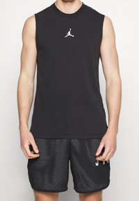 Canottiera nera senza maniche in cotone, con un piccolo logo Jumpman bianco sul petto, abbinata a pantaloni corti in rete neri.