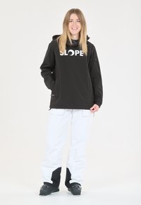 Veste imperméable noire avec le logo blanc "SLOPE", associée à un pantalon cargo blanc avec des accents noirs et des poches pratiques.
