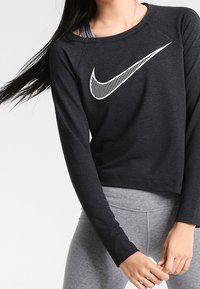 Maglione cropped nero realizzato in materiale morbido, con il logo bianco di Nike sulla parte anteriore. Maniche lunghe e scollo rotondo visibili.