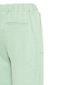 Pantalon vert clair à taille élastique avec poche passepoilée à l'arrière et couture latérale, fabriqué en tissu texturé.