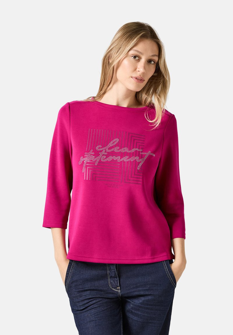 Pull en fuchsia à manches trois quarts, doté d'un imprimé graphique texturé en argent à l'avant. Tissu doux, coupe décontractée et fentes sur les côtés.