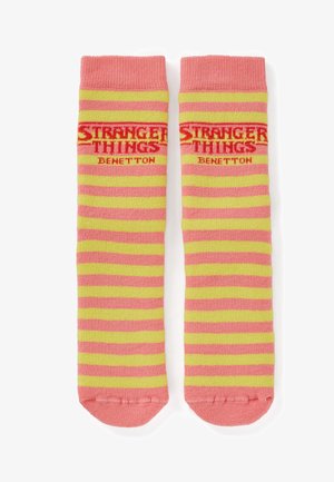 Roze en geel gestreepte sokken met de teksten "STRANGER THINGS" en "BENETTON", gebreide textuur en geribbelde boorden met een afgeronde teen.