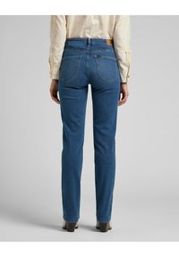 Jeans blu scuro con un design aderente, caratterizzati da vita alta, tasche posteriori e dettagli di cucitura minimali. Texture piatta e taglio classico.