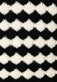 Strickstoff mit einem Zickzackmuster in abwechselndem Schwarz und Weiß. Die Textur ist weich mit sichtbaren Schlaufen und erhabenen Bereichen.