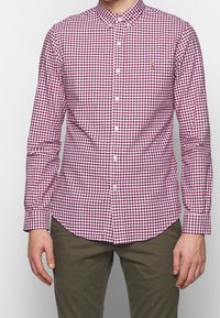 Long-sleeve button-up shirt in red and white gingham pattern, featuring a classic collar and front button closure, made from fabric with a smooth texture.