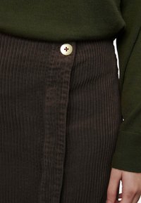 Bruine corduroy rok met verticale ribbels, een zijsluiting met een decoratieve kruisknop, gecombineerd met een groen gebreid top.