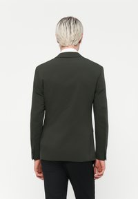 Mørkegrøn blazer lavet af glat stof, med et struktureret design, enkelt ventilation bagpå og knapmanchetter.