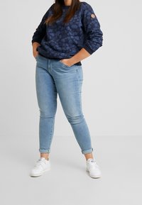 Sudadera azul marino con estampado floral y puños acanalados, combinada con jeans skinny de color azul claro y zapatillas blancas.