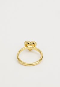 Goldring mit herzförmigem Oberteil, das ein lächelndes Design zeigt, akzentuiert mit einem kleinen Edelstein am Band, glatte Textur und glänzende Oberfläche.