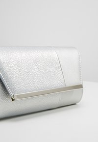 Borsa a tracolla argento con una finitura testurizzata, caratterizzata da una sezione liscia e un accento metallico sulla patta anteriore.