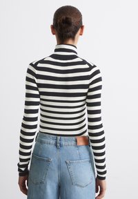 Zwart-wit gestreepte coltrui met lange mouwen, gecombineerd met lichtblauwe high-waisted denim jeans met achterzakken en een leren logo label.