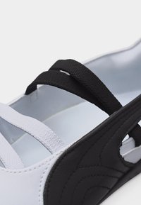 Κοντινή λήψη ενός ασπρόμαυρου σανδαλιού που δείχνει υφασμάτινες λωρίδες με υφή και ραμμένα πάνελ από συνθετικό δέρμα.