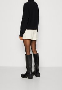 Zwarte kniehoge laarzen met een glanzende leren afwerking, dikke plateauzolen en een gladde textuur, gecombineerd met een lichtgekleurde rok.