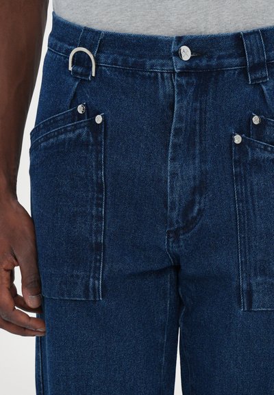 Pantalones de denim azul oscuro con corte recto, dos bolsillos frontales con herrajes plateados y un lazo para accesorios en la cintura.