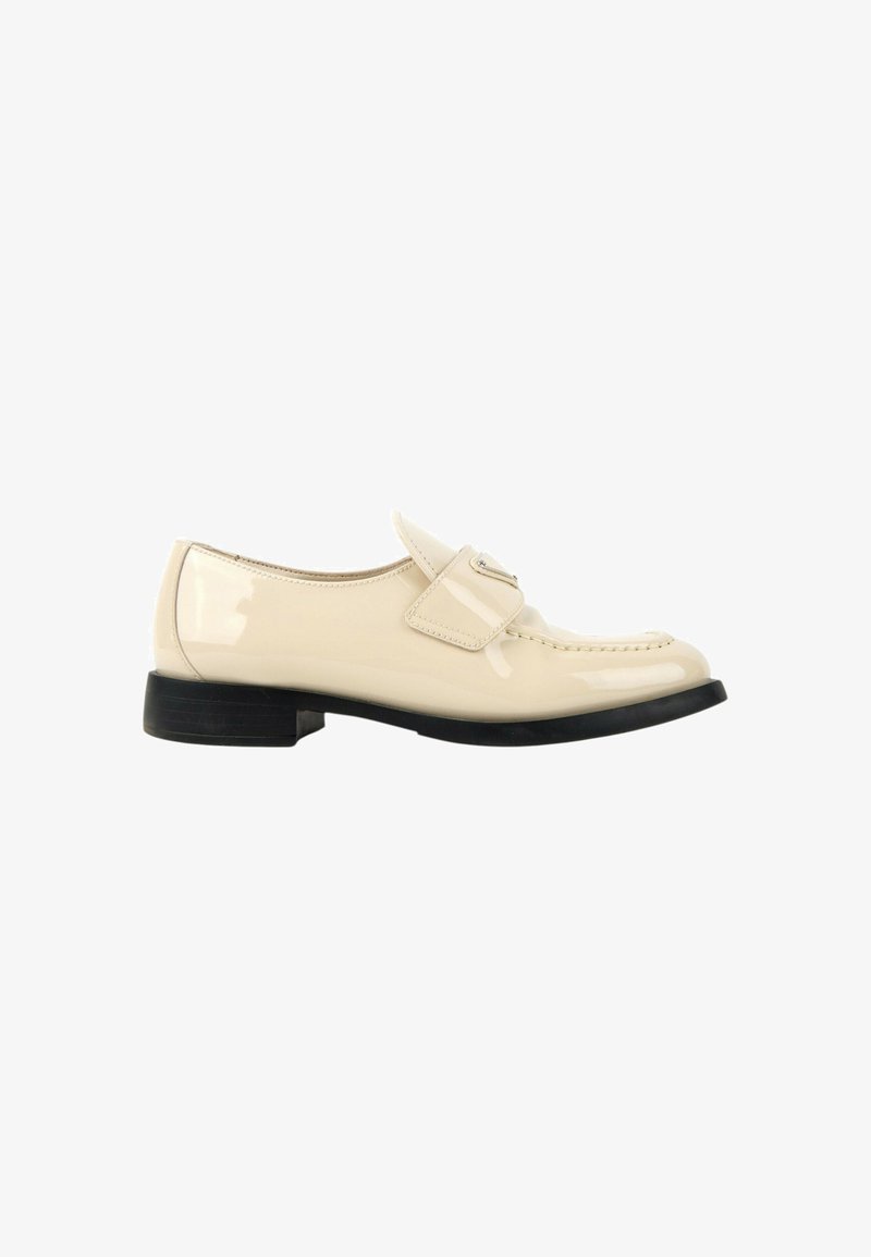 Mocassin crème brillant avec une bride et une petite boucle, petit talon et semelle noirs, vu de côté sur fond blanc.