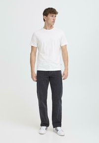 Camiseta blanca de manga corta combinada con jeans gris oscuro. El modelo está de pie sobre un fondo sencillo, mostrando un atuendo casual con zapatillas blancas.