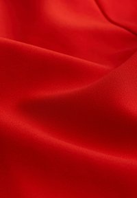 Leuchtend roter Stoff mit einer glatten Textur, der dezente Falten und einen leichten Glanz zeigt. Das Material wirkt leicht und fein.