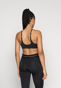 Fekete sportmelltartó állítható pántokkal, sima anyagból, U-alakú háttal. Magas derekú leggingsszel párosítva, amely kontrasztos derékrésszel rendelkezik.